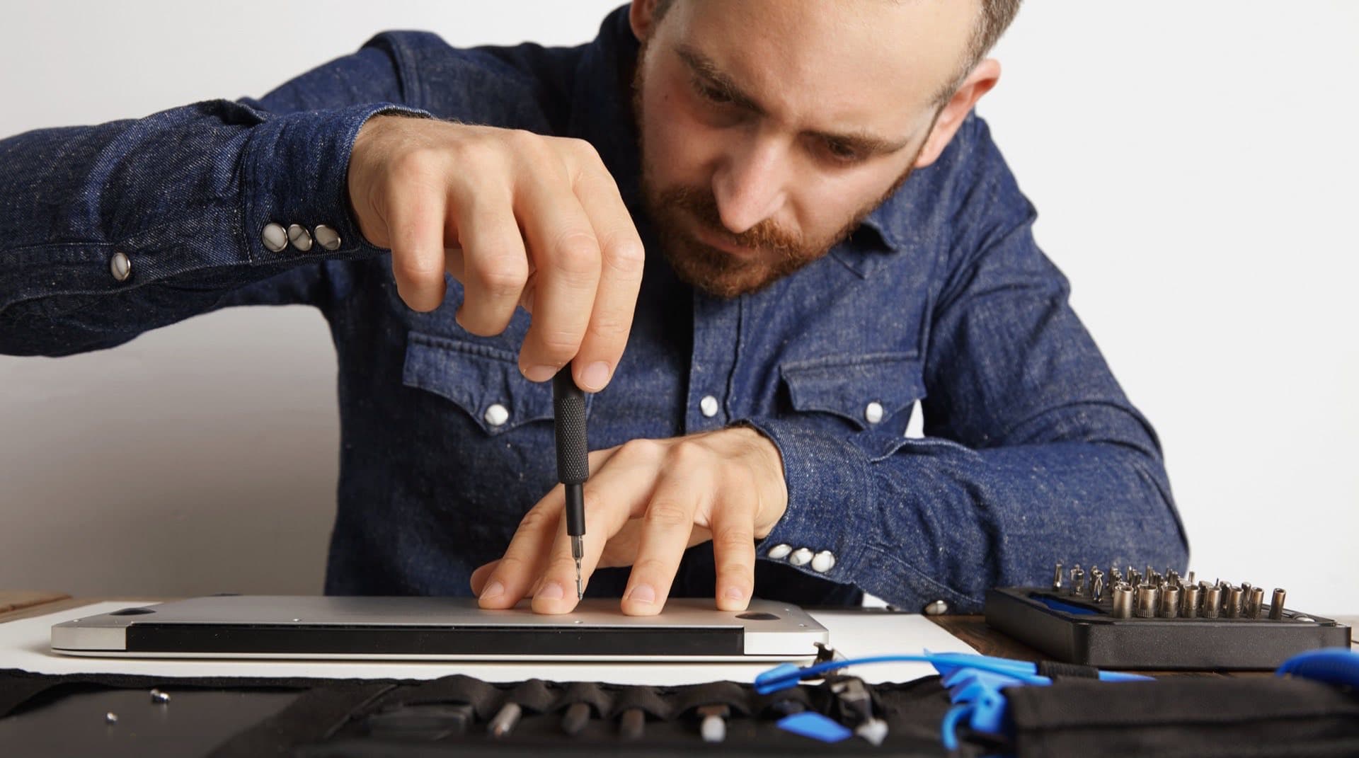 A refurbished laptop on a clean workbench beside a precision screwdriver and microfibre cloth